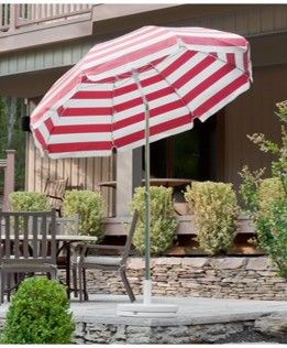 Red and white commercial patio umbrella with weighted base beside outdoor dining furniture on a residential-style patio deck